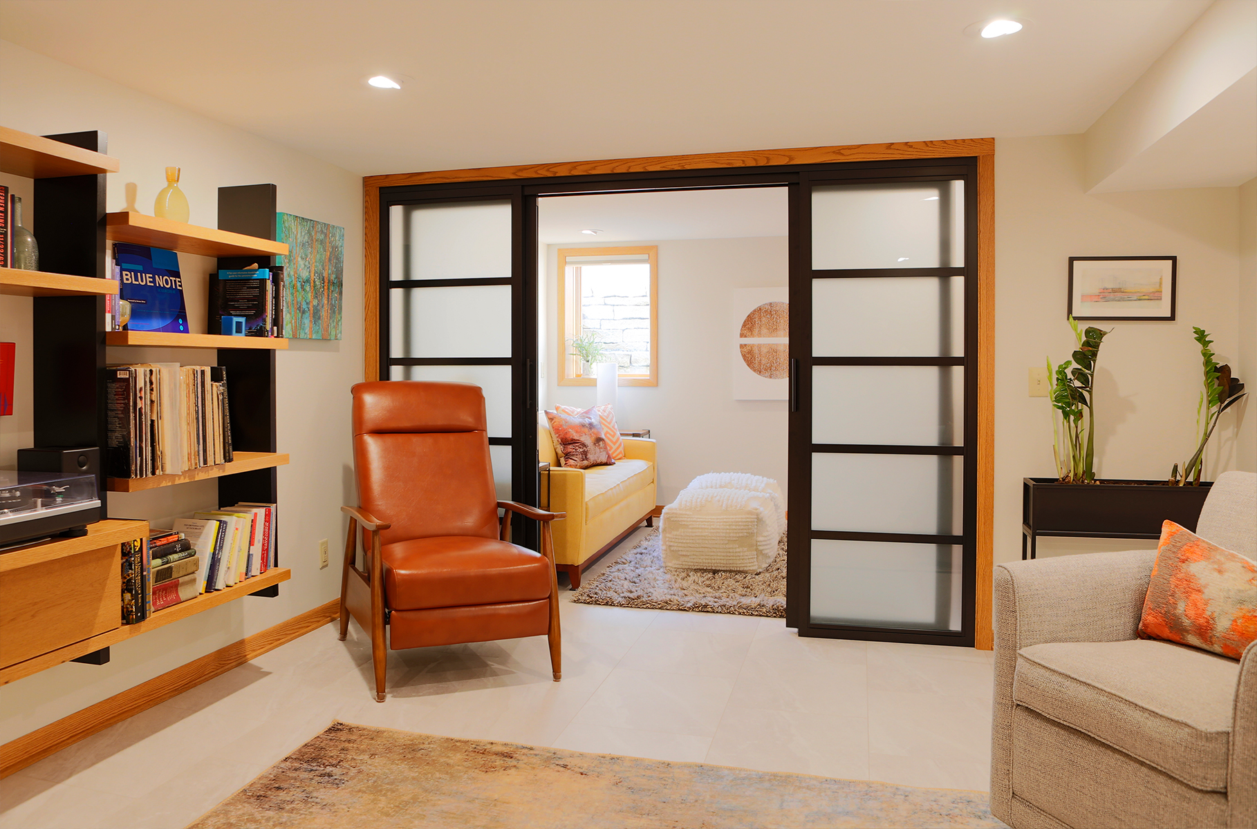 A full color image of a lower level entertaining space with built-in shelves and sliding doors opening to a guest suite