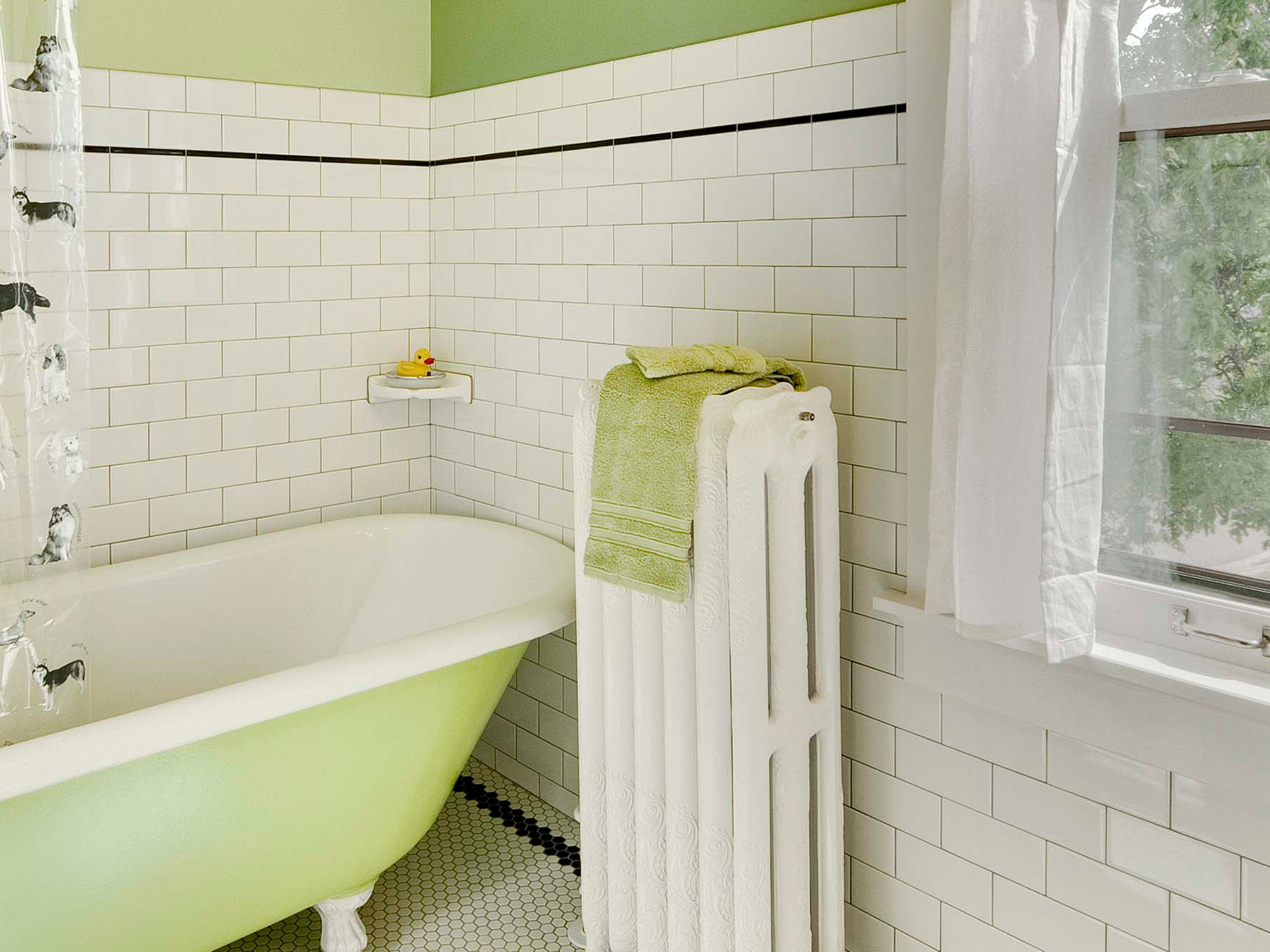 A full color after remodel image of a bathroom with white tile walls, a painted claw foot tub with a white painted radiator