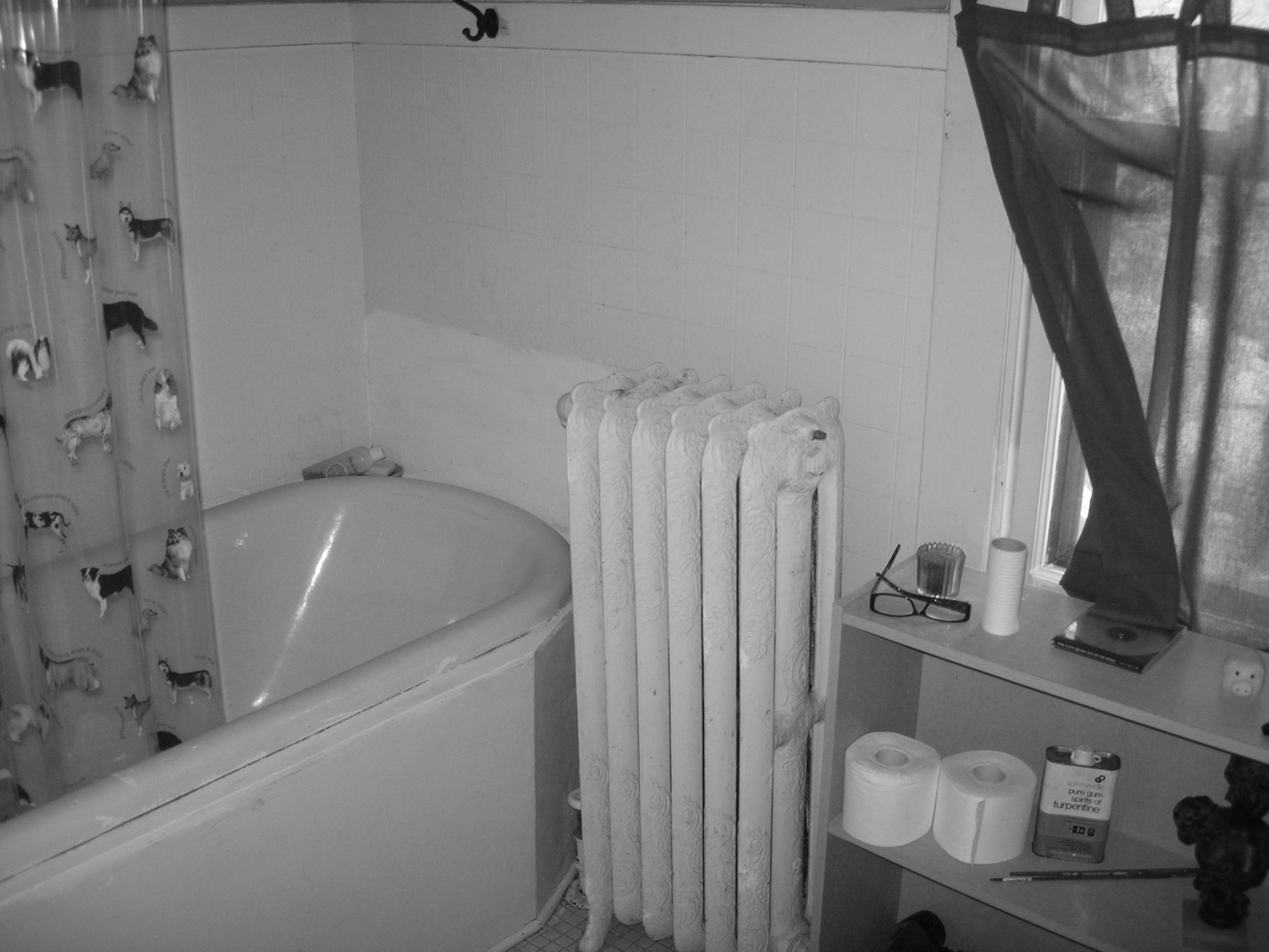 A before remodel image of a bathroom with a tub and radiator, captured in black and white